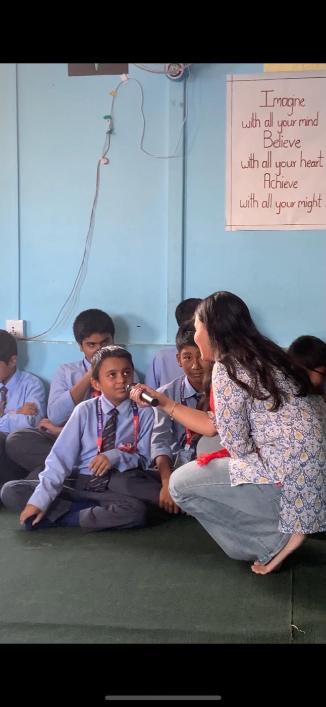 Alisha holding a microphone to a young student sharing his answer during a school session